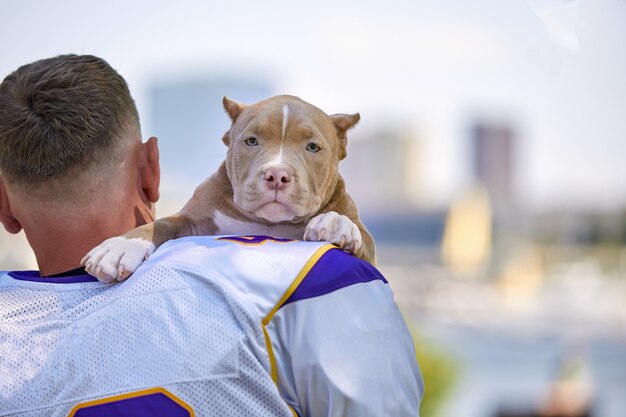 Spieler des amerikanischen Fußballs mit einem Hund, der auf Kamera in einem Park aufwirft. Exemplar, Sportfahne. American Football, Sport zum Schutz der Tiere.