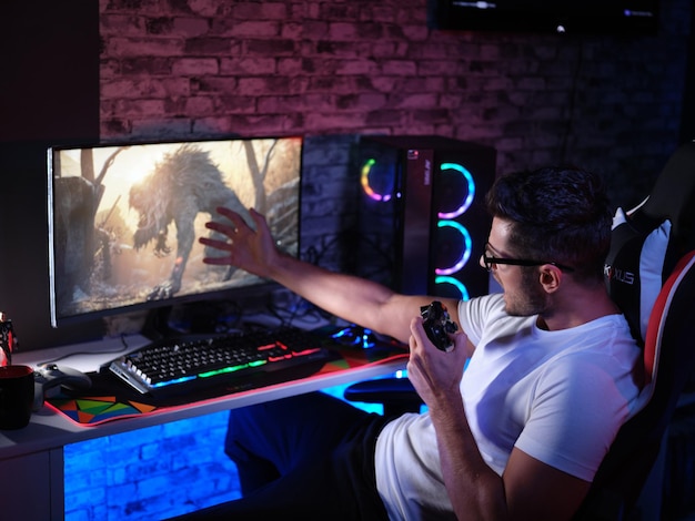 Spieler imitiert mit einer Hand eine Kreatur auf dem Bildschirm, umgeben von lebhaft beleuchteten Gaming-Geräten