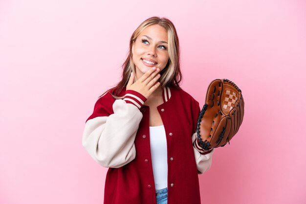Spieler Russische Frau mit Baseballhandschuh isoliert auf rosa Hintergrund, die lächelnd aufblickt