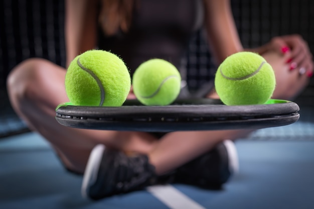 Spielerin mit Tennisschläger und Bällen, die am Netz sitzen