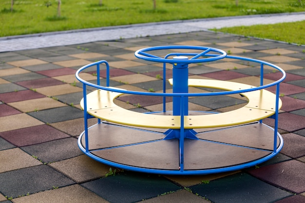 Spielplatz im kindergarten mit weichem bodenbelag und buntem hellem karussell draußen.