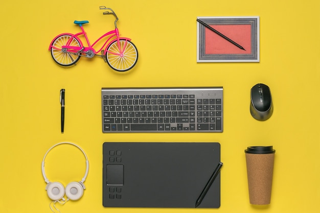Spielzeug Fahrrad, Bild, Tastatur und Grafiktablett auf gelbem Grund. Designer-Arbeitsplatz.