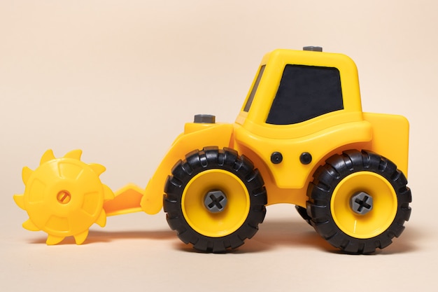 Spielzeug gelber Traktor mit runder Sägedüse für Holz auf beigem Hintergrund