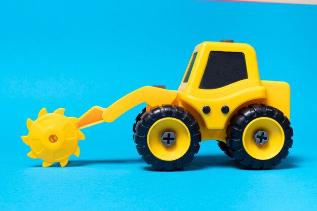 Spielzeug gelber Traktor mit runder Sägedüse für Holz auf blauem Grund.
