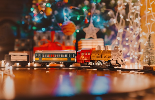 Spielzeug Vintage Dampflokomotive auf dem Boden unter einem verzierten Weihnachtsbaum auf einem Hintergrund der Bokeh Lichter Girlande