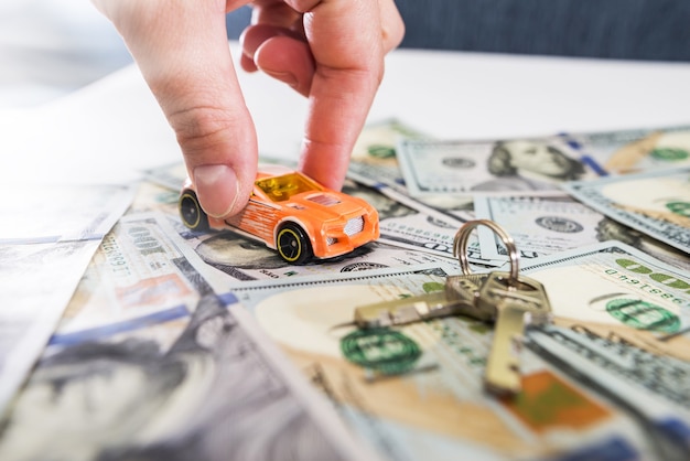 Spielzeugauto in der Hand, Schlüssel und Geld auf dem Tisch.