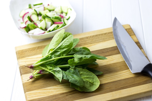 Spinat auf einem Holzbrett schneiden. Salat aus Gurke, Rettich und Spinat.