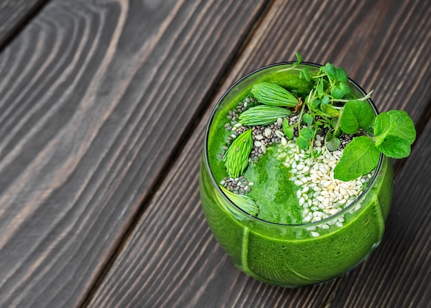 Spinat-Smoothie mit Früchten und Samen, dekoriert mit Minzblättern, einer Limettenscheibe und wilden Blumen in einer Glasschale