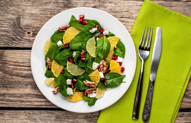 Spinatsalat, Orange, Zitrone, Granatapfel, Fetokäse, Walnuss auf einem weißen Teller auf einem Holztisch