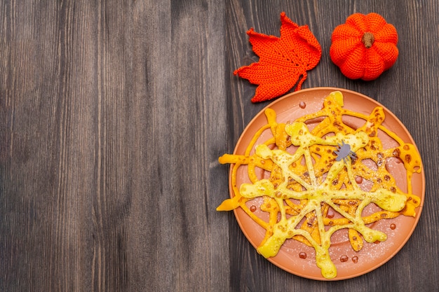 Spinnennetzpfannkuchen mit Zuckersirup und -pulver zum Halloween-Frühstück. Mit gehäkeltem Orangenkürbis und Blatt