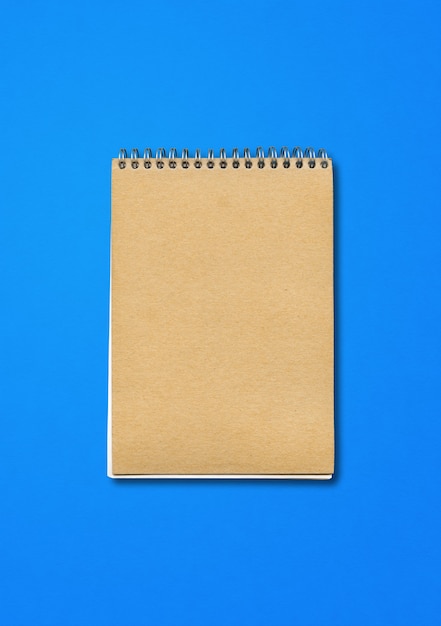 Spiral geschlossenes Notizbuchmodell, braune Papierabdeckung, lokalisiert auf blauem Hintergrund