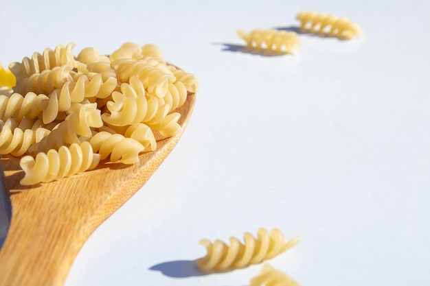 Spiralnudeln liegen in einem Holzlöffel auf einem weißen Tisch Das Konzept der Kochgastronomie