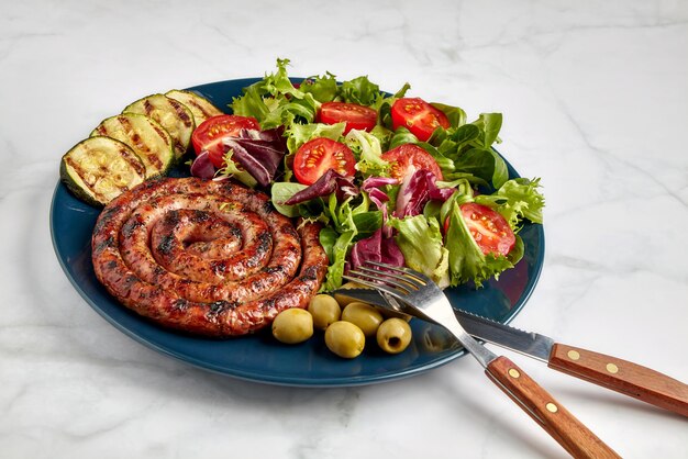 Spiralwurstgrill mit geschnittenen Tomaten, Zucchini und Salat auf einer blauen Platte auf einem Leuchttisch