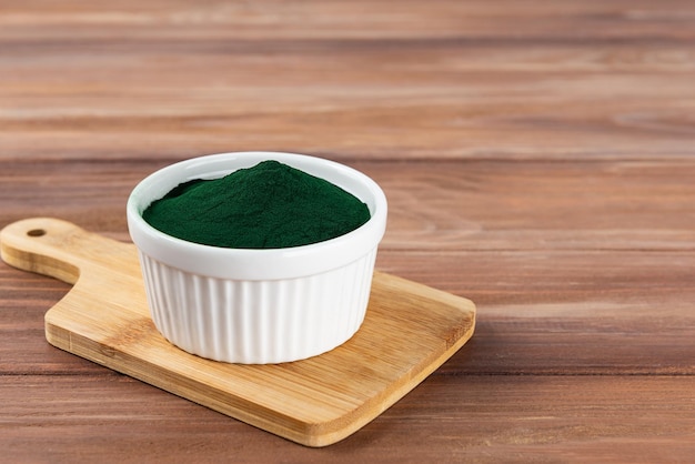 Spirulina em pó em uma tigela em uma placa de madeira