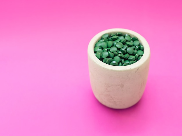 Spirulina havaiana verde em pílulas de colher de sopa em fundo rosa Superalimento estilo de vida saudável