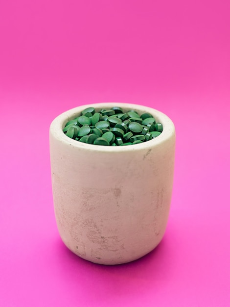 Spirulina havaiana verde em pílulas de colher de sopa em fundo rosa Superalimento estilo de vida saudável