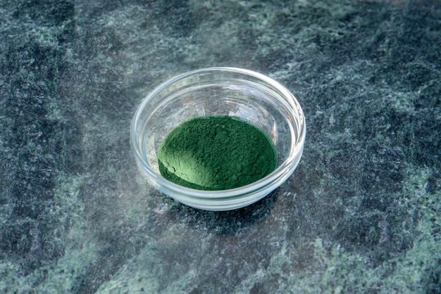 Spirulina-Pulver in einer Glasschale auf grünem Marmorhintergrund.