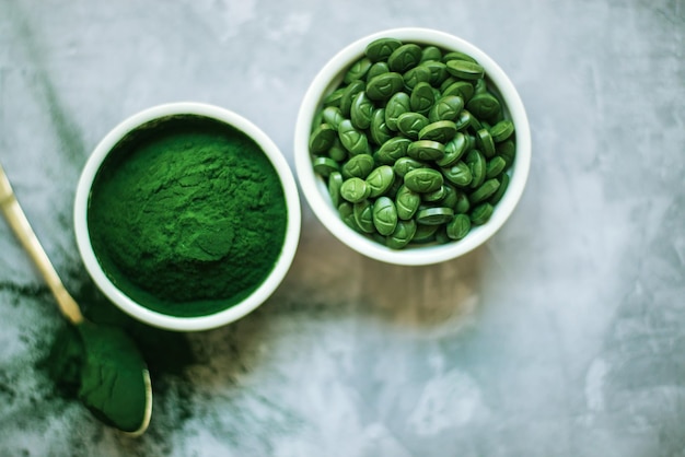 Spirulina-Pulver und Tabletten in weißen Platten auf Betongrund