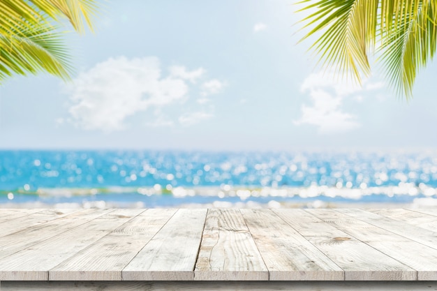 Spitze der hölzernen Tabelle mit Meerblick und Palmblättern, Unschärfe bokeh Licht von ruhigem See und Himmel am tropischen Strand