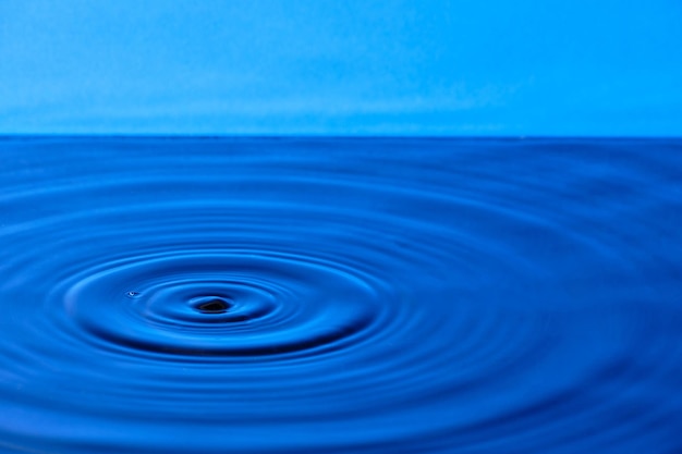 Splash Wassertropfen mit divergierenden Wasserkreisen auf blauem Hintergrund