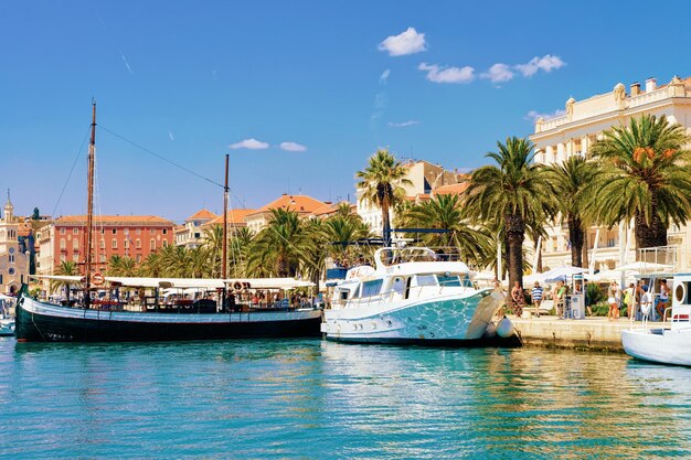 Foto split, croácia - 16 de agosto de 2016: navios em palmeiras na cidade velha de split, na costa do adriático, na dalmácia, na croácia. arquitetura do palácio de diocleciano e da cidade romana na baía da dalmácia croata