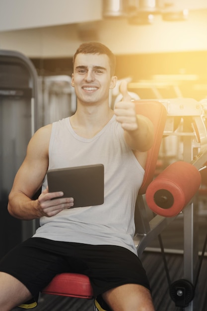 sport, bodybuilding, lifestyle, technologie und personenkonzept - lächelnder junger mann mit tablet-pc-computer im fitnessstudio