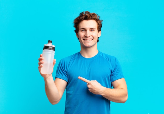 Sport boy sonriendo alegremente, sintiéndose feliz y apuntando hacia un lado y hacia arriba, mostrando el objeto en el espacio de la copia. concepto de bebida energética