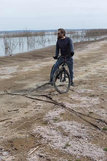 Sport brutaler bärtiger Kerl auf einem modernen Mountainbike Ein Radfahrer an einem salzwüsten Ort am See