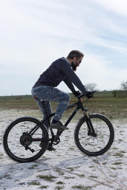 Sport brutaler bärtiger Kerl auf einem modernen Mountainbike Ein Radfahrer an einem salzwüsten Ort am See