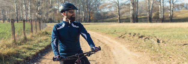 Sport brutaler bärtiger Kerl auf einem modernen Mountainbike Radfahrer auf den grünen Hügeln im Frühjahr