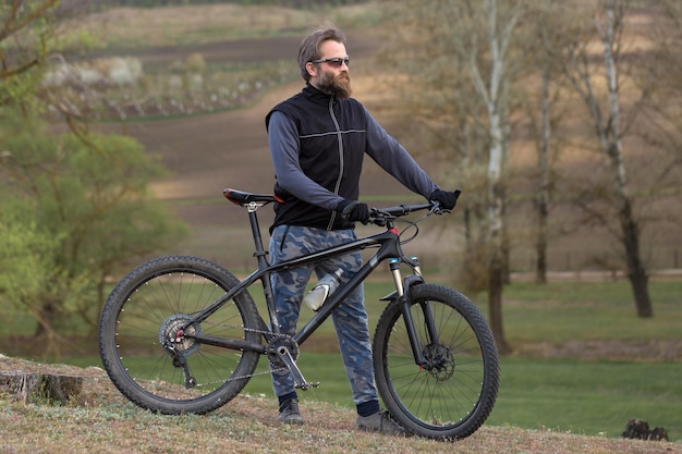 Sport brutaler bärtiger Kerl auf einem modernen Mountainbike-Radfahrer auf den grünen Hügeln im Frühjahr