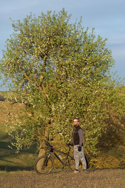 Sport brutaler bärtiger Kerl auf einem modernen Mountainbike-Radfahrer auf den grünen Hügeln im Frühjahr