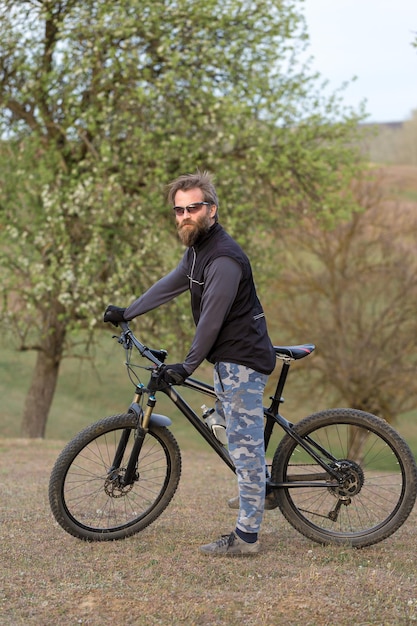 Sport brutaler bärtiger Kerl auf einem modernen Mountainbike-Radfahrer auf den grünen Hügeln im Frühjahr