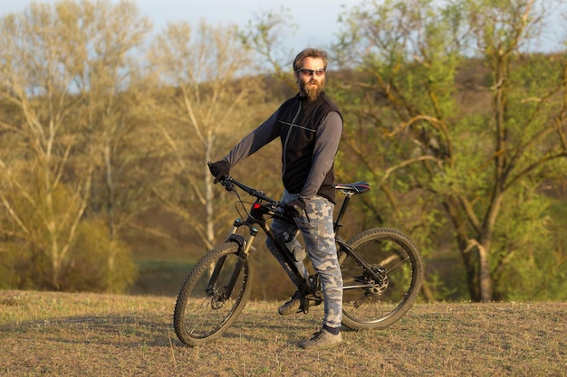 Sport brutaler bärtiger Kerl auf einem modernen Mountainbike-Radfahrer auf den grünen Hügeln im Frühjahr