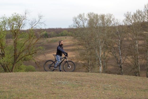 Sport brutaler bärtiger Kerl auf einem modernen Mountainbike-Radfahrer auf den grünen Hügeln im Frühjahr