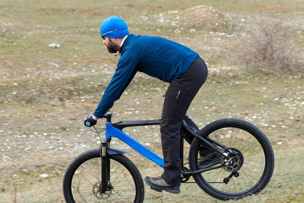 Sport brutaler bärtiger Kerl auf einem modernen Mountainbike. Radfahrer auf den grünen Hügeln im Frühjahr.