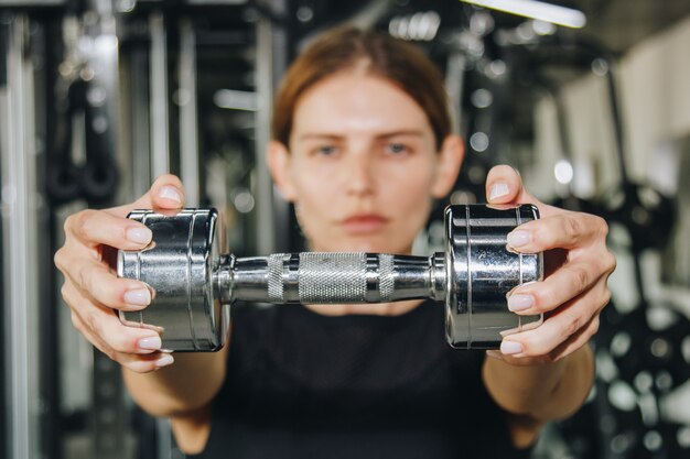 Sport, Eignung, Bodybuilding, Gewichtheben und Leutekonzept - nah oben von der Frau, die Arme mit Dummkopf in der Turnhalle biegt.