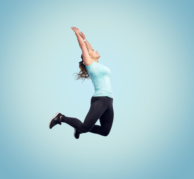 Foto sport-, fitness-, bewegungs- und personenkonzept - glücklich lächelnde junge frau, die in die luft springt oder auf blauem hintergrund tanzt