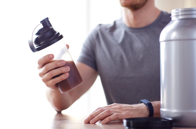 sport, fitness, gesunder lebensstil und personenkonzept - nahaufnahme des mannes im fitnessarmband mit glas und flasche, die proteinshake zubereitet