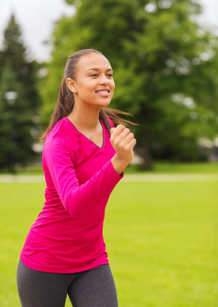 Sport, Fitness, Gesundheit und People-Konzept - lächelnde junge afroamerikanische Frau, die im Freien läuft