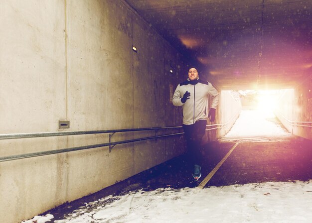 Foto sport-fitness-leute saison und gesunder lebensstil konzept glücklicher junger mann läuft entlang fußgänger u-bahn-tunnel im winter