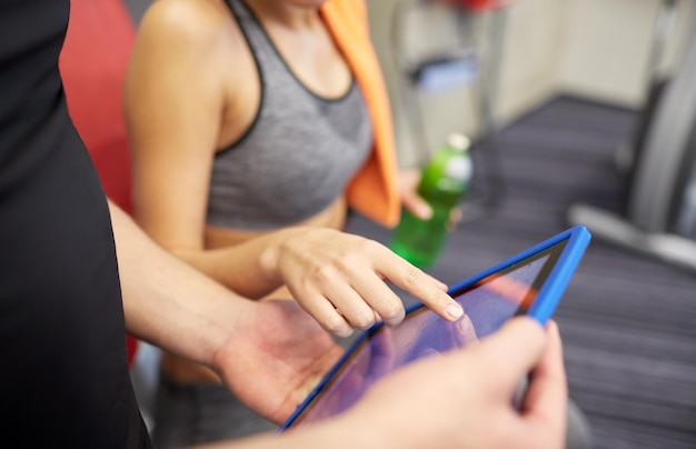 Sport-, Fitness-, Lifestyle-, Technologie- und People-Konzept - Nahaufnahme von Trainerhänden mit Tablet-PC-Computer und Frau, die im Fitnessstudio trainiert