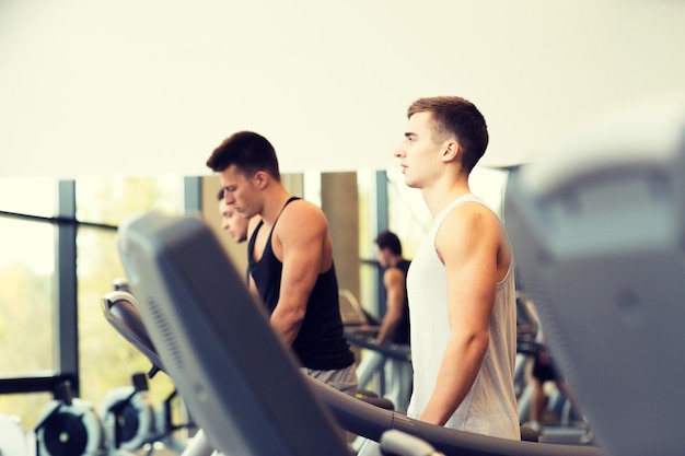 sport, fitness, lifestyle, technologie und personenkonzept - gruppe von männern, die auf dem laufband im fitnessstudio trainieren