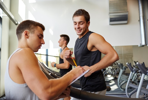 sport, fitness, lifestyle, technologie und personenkonzept - männer mit personal trainer trainieren auf laufband im fitnessstudio