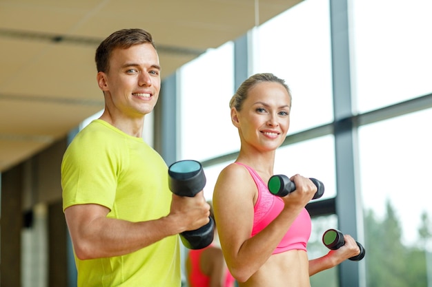 sport, fitness, lifestyle und people concept - lächelnder mann und frau mit hanteln, die im fitnessstudio trainieren