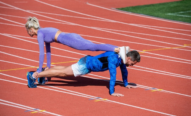 Sport-Fitness-Mann und -Frau, die zusammen trainieren, stehen in Planke und drücken auf der Outdoor-Stadion-Rennstrecke mit Sportbekleidung, gesundem Lebensstil.
