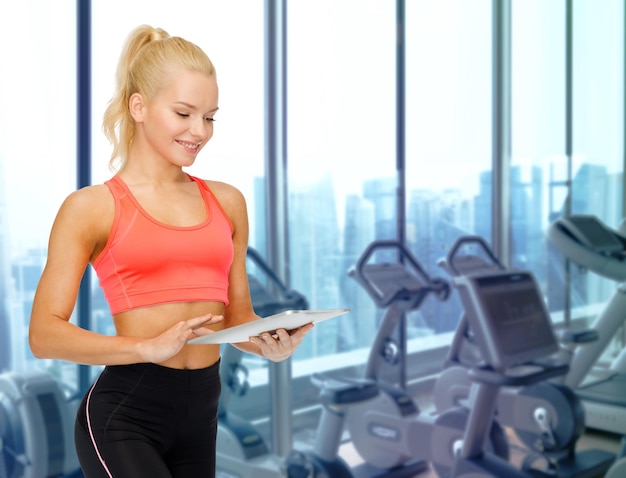 sport, fitness, technologie, werbung und personenkonzept - lächelnde sportliche frau mit tablet-pc-computer über fitnessgerätehintergrund