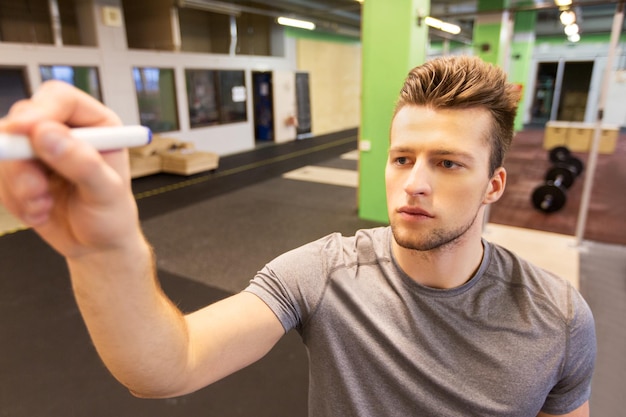 Sport-, Fitness- und People-Konzept – Mann schreibt Notizen an Whiteboard im Fitnessstudio