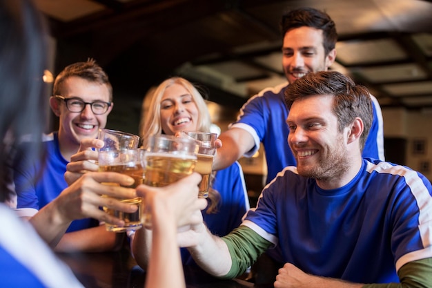 Sport-, Fußball-, Menschen- und Freizeitkonzept - glückliche Freunde oder Fußballfans, die mit Biergläsern klirren und den Sieg in der Bar oder Kneipe feiern