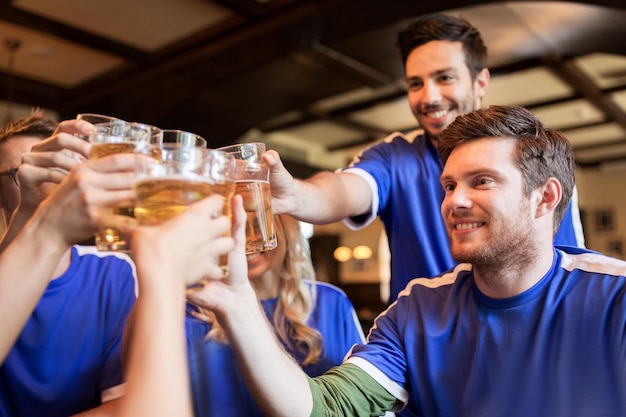 Sport-, Fußball-, Menschen- und Freizeitkonzept - glückliche Freunde oder Fußballfans, die mit Biergläsern klirren und den Sieg in der Bar oder Kneipe feiern